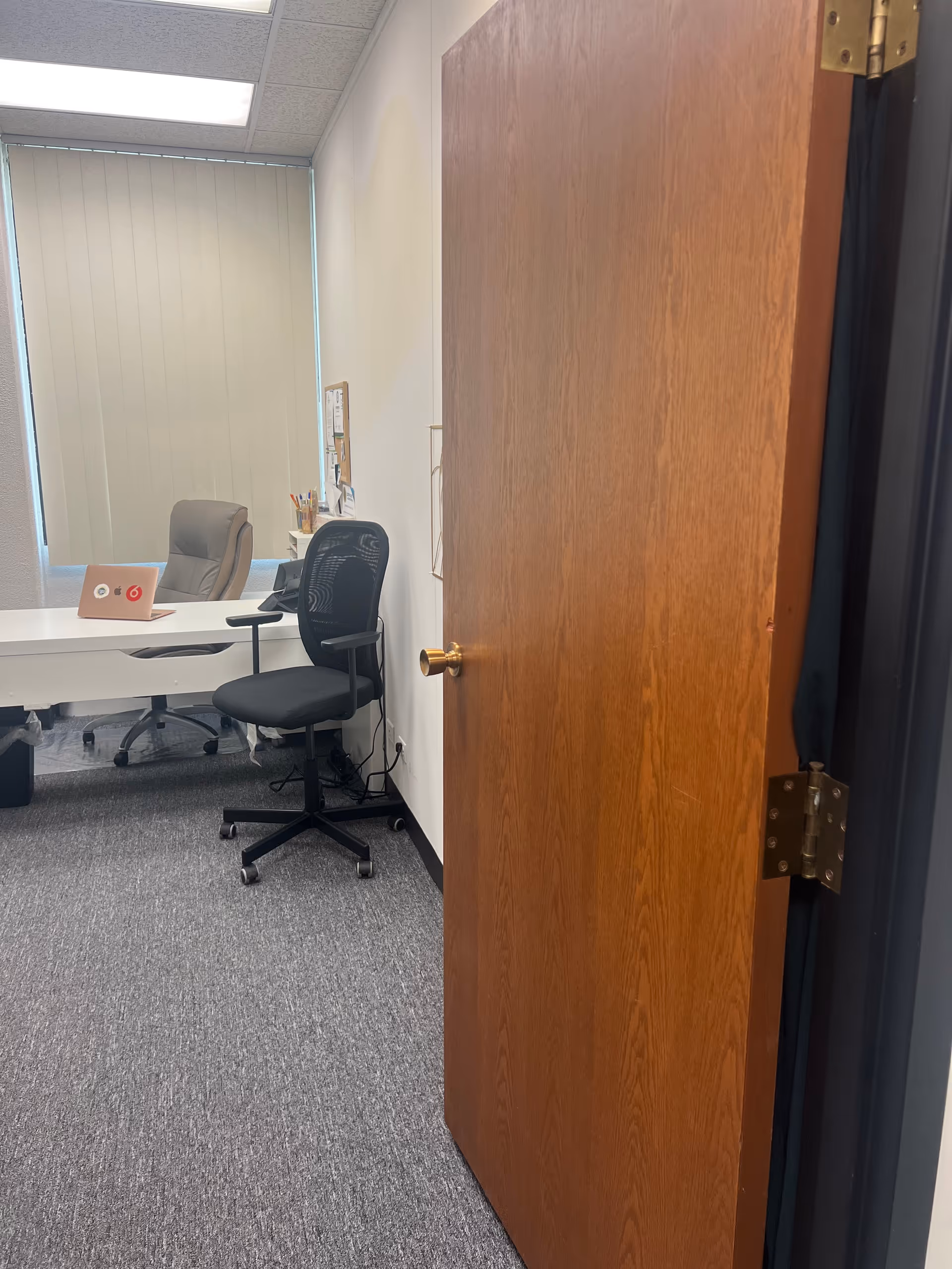 Open wooden door reveals a small office with desk, chair, and supplies.