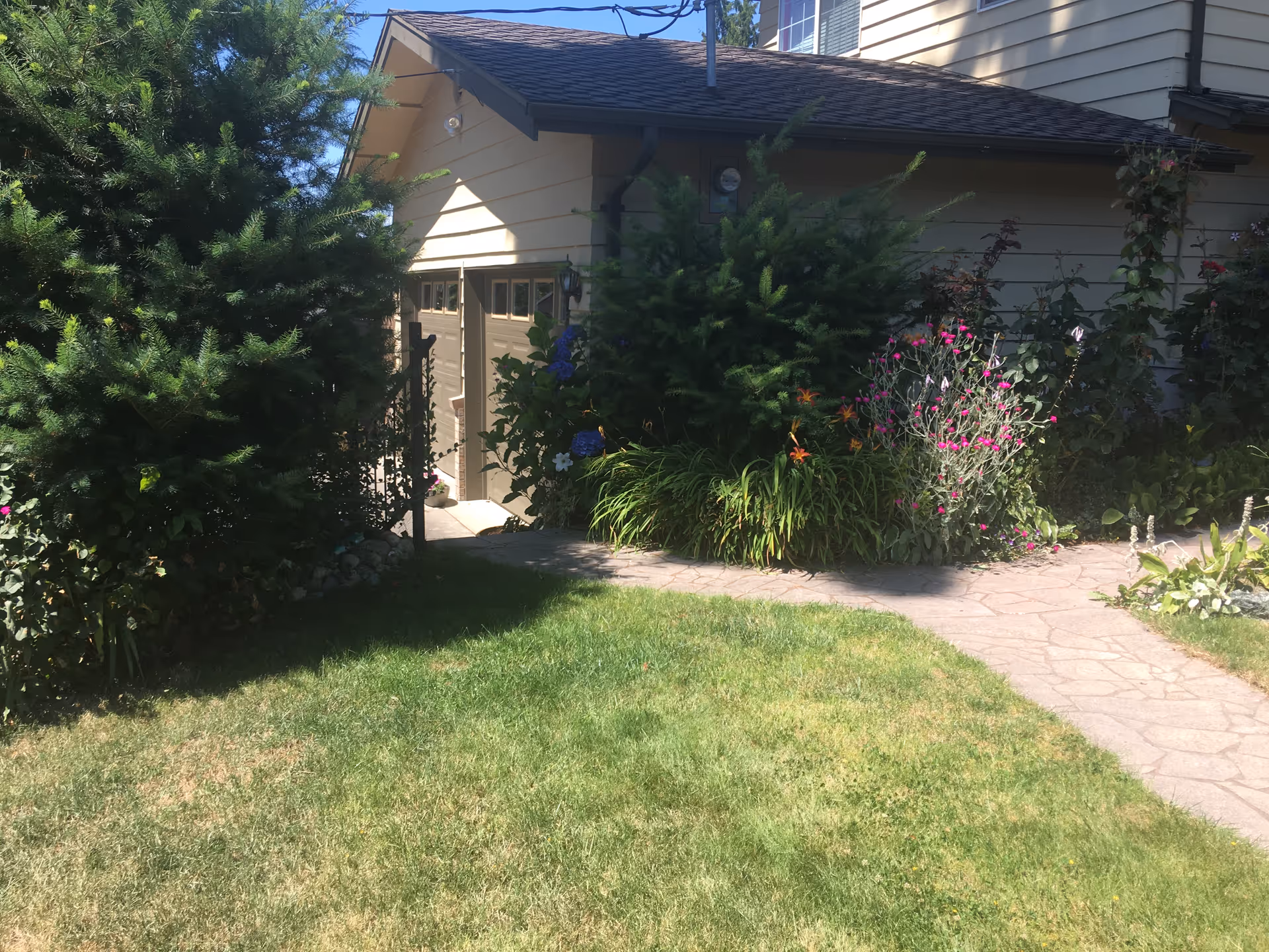 Front-yard exterior of a home with a stone path, lawn, and flowering shrubs.