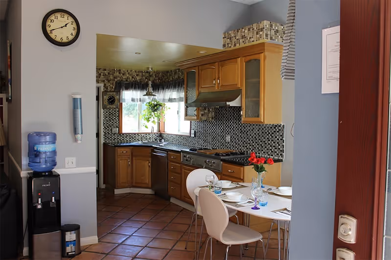 A compact kitchen with wooden cabinets, mosaic backsplash, and a dining table set for a meal.