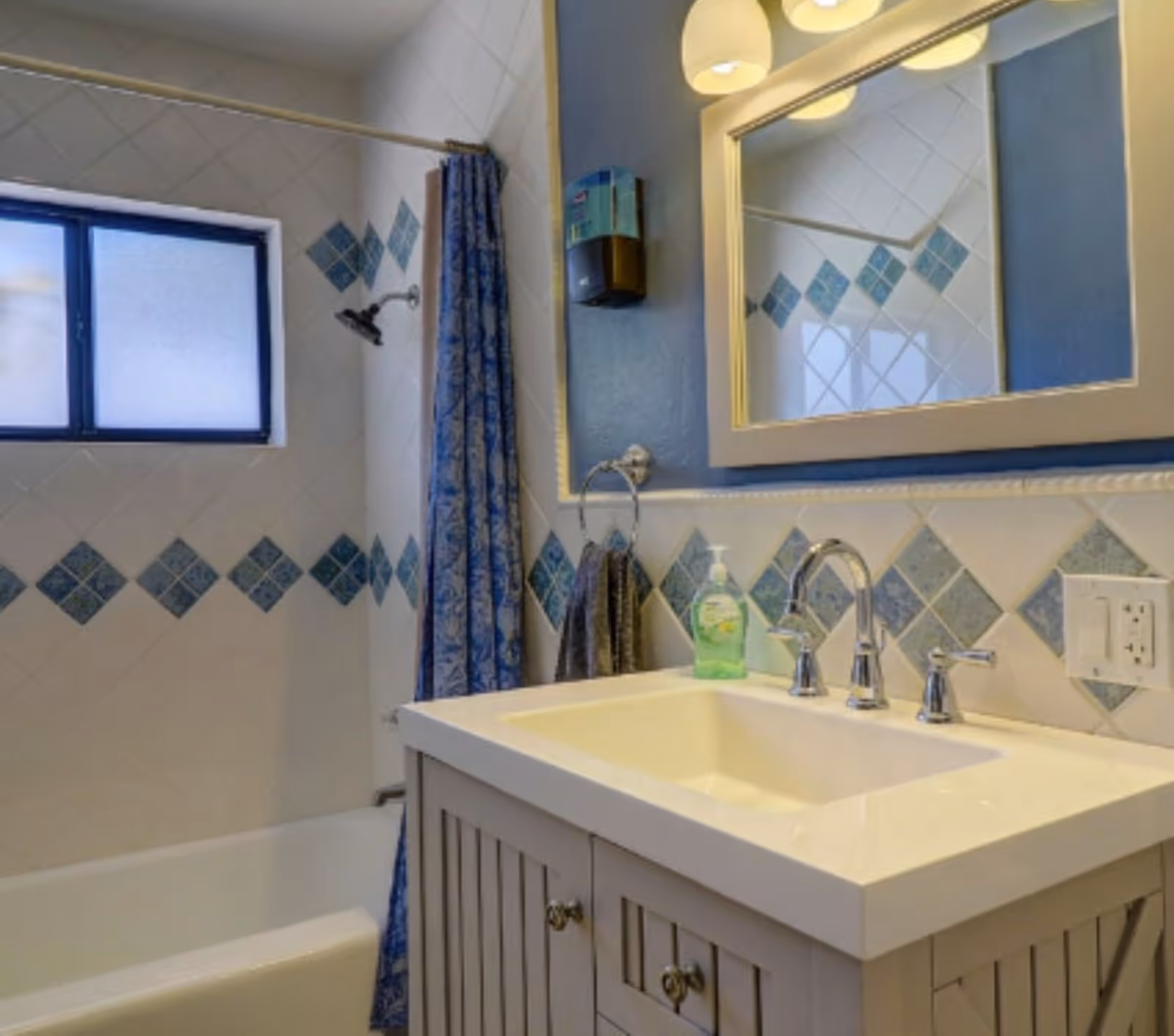 Bathroom interior with sink, mirror, blue diamond tile backsplash, shower curtain, and tub.