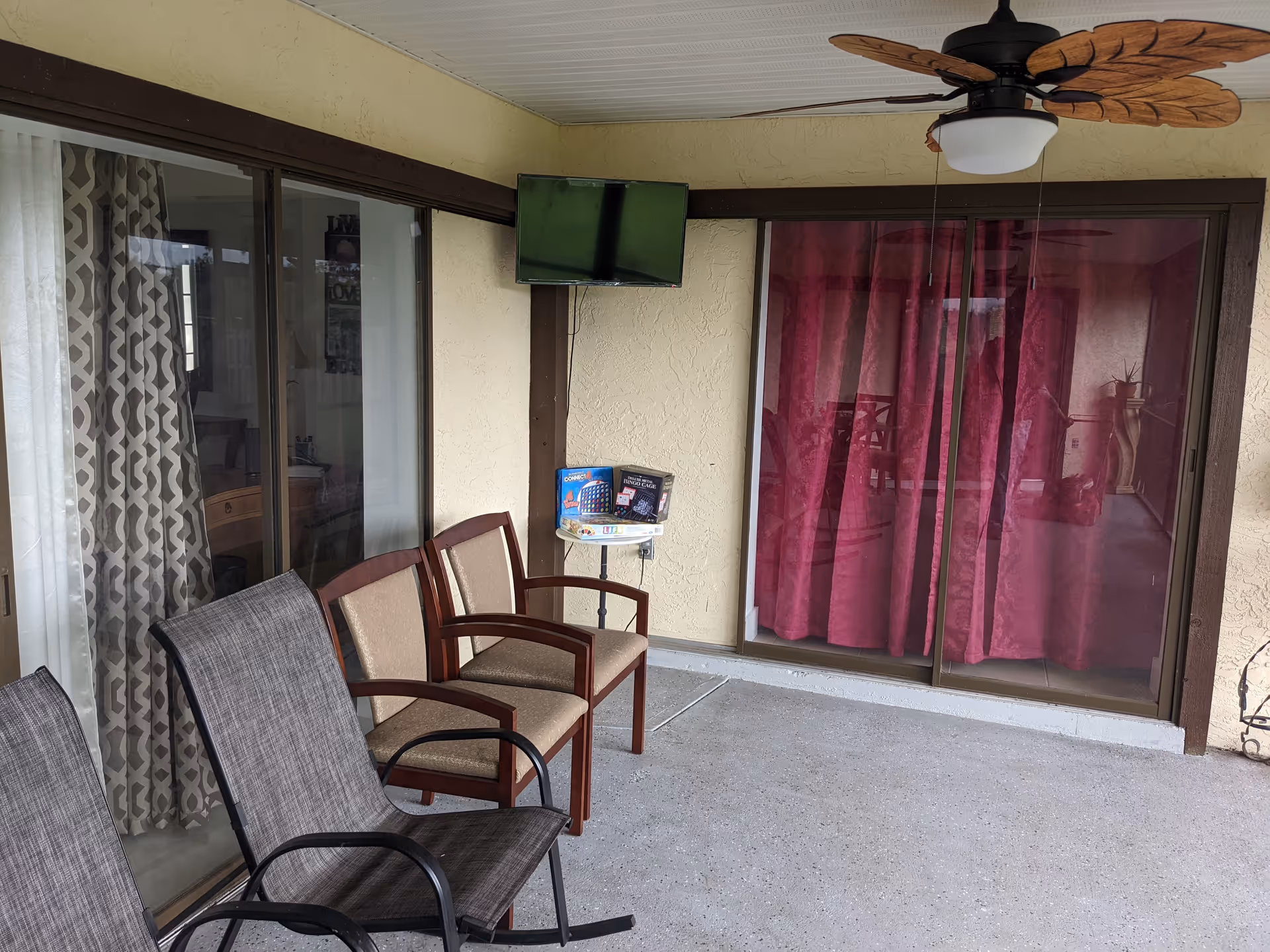 Outdoor patio area with chairs, a small table, TV, and pink curtains.
