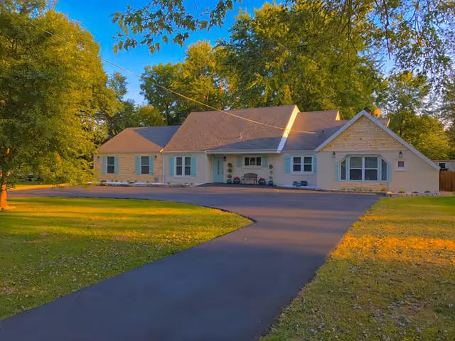 Front view of a single-story senior living facility with a curved driveway and trees.
