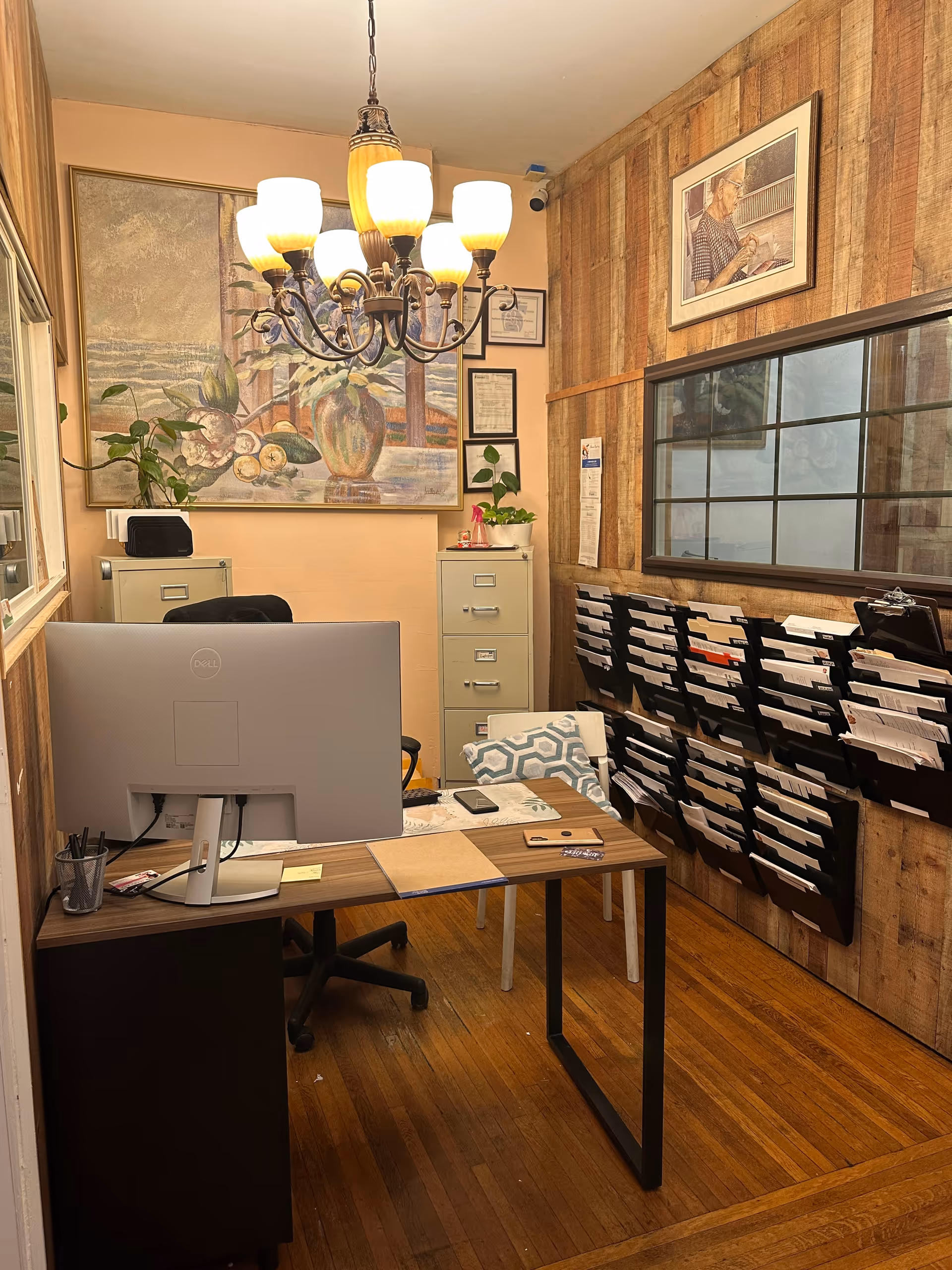 Office workspace inside a senior living facility with desk, computer, filing cabinets, and wall art.