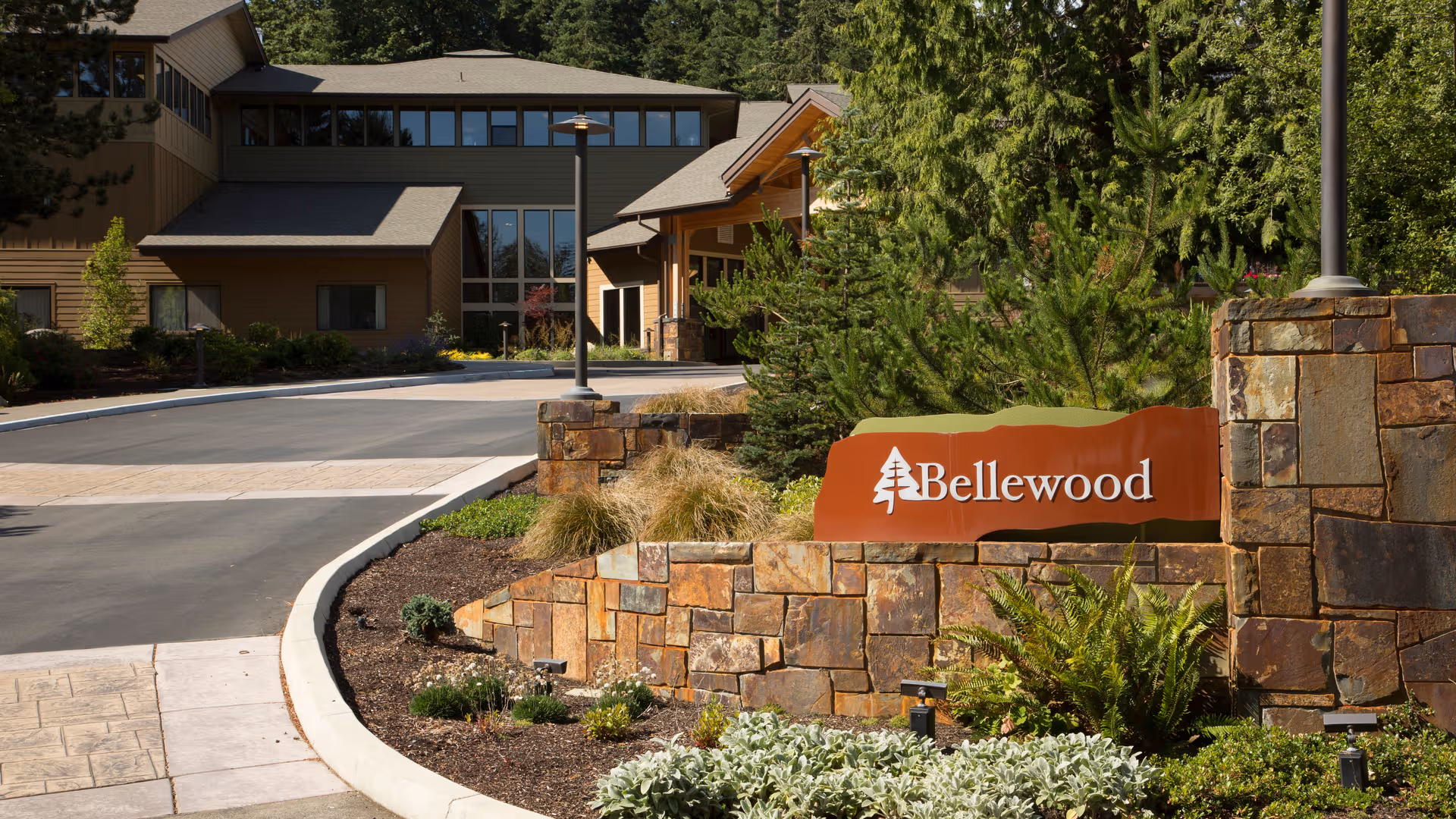 Exterior view of Bellewood entrance with stone sign, landscaped beds, and a modern building.