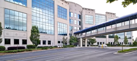 Modern multi-story cancer care facility exterior with glass façade and skybridge.