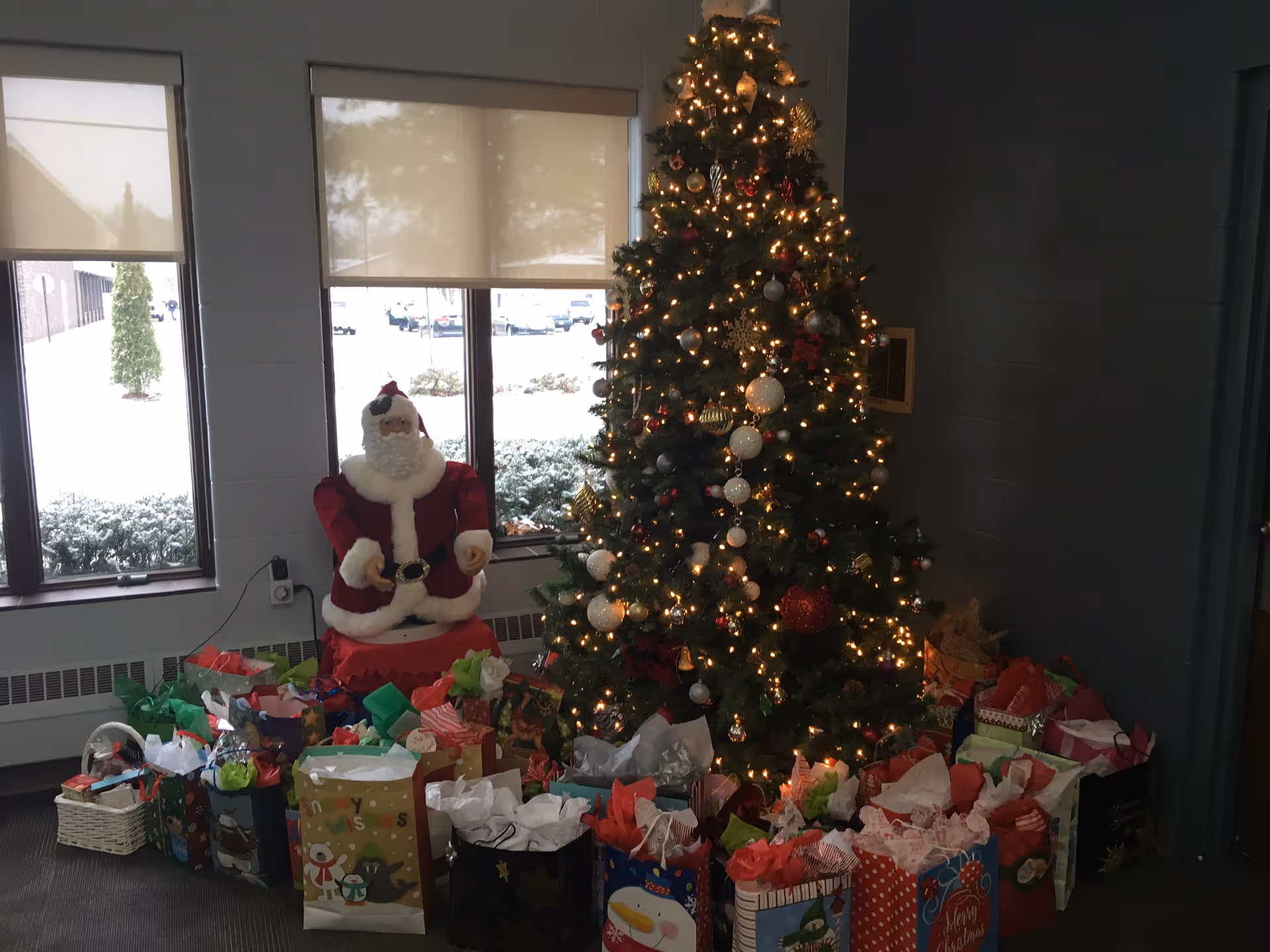 A decorated Christmas tree, Santa figure, and numerous gift bags in a senior living lobby.