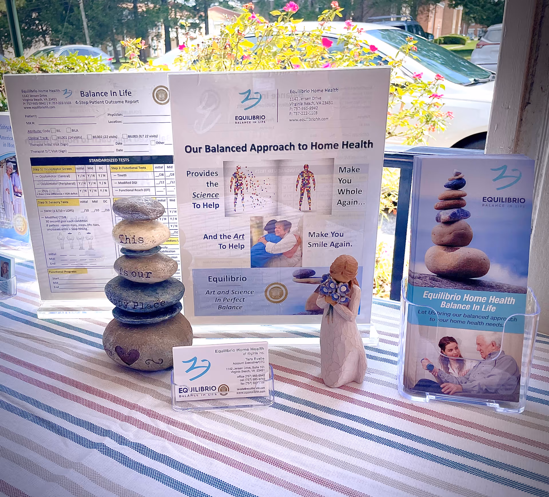 Outdoor promotional display for Equilibrio Home Health with posters, brochures, and stacked stone sculpture.