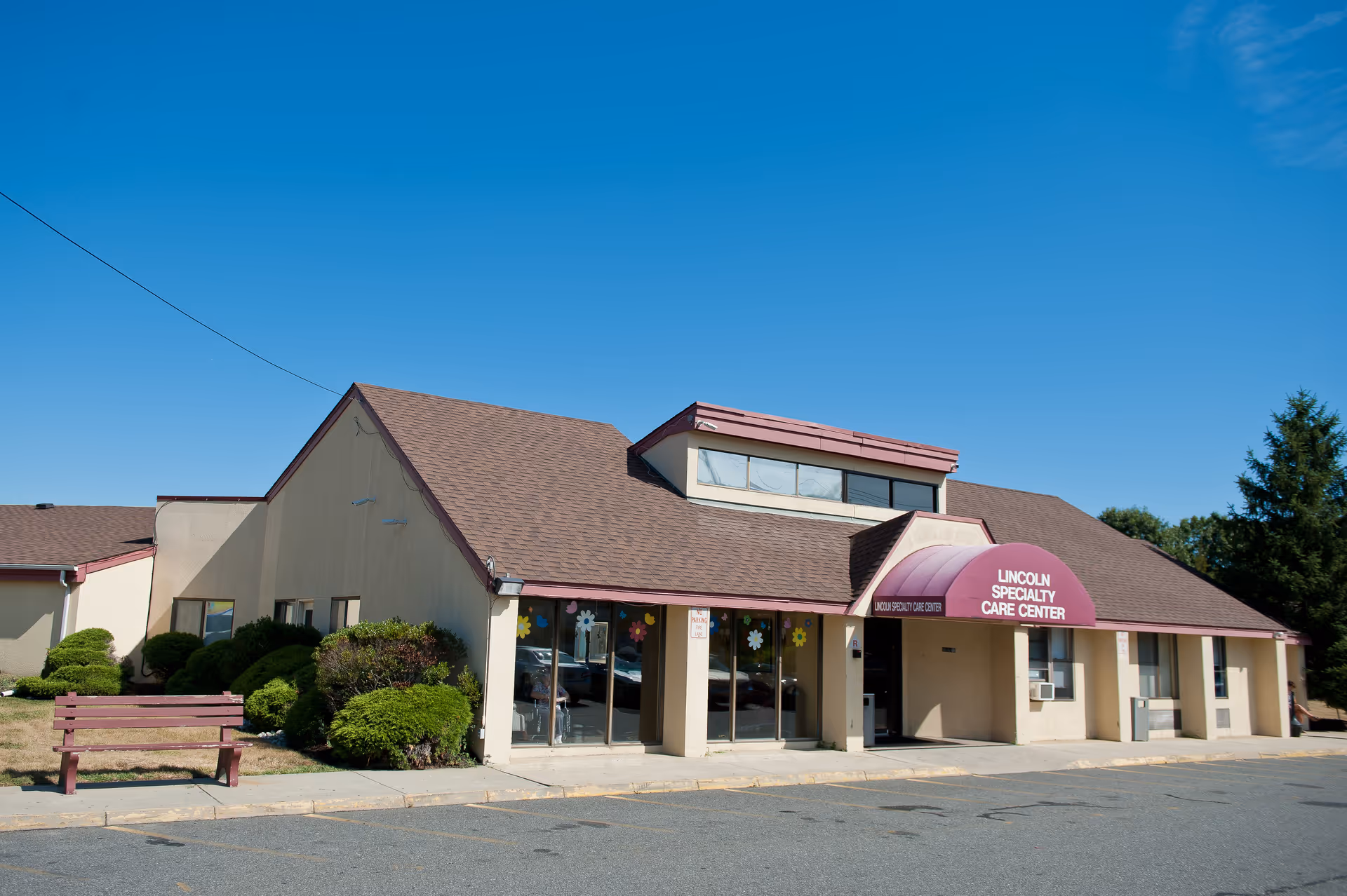 Single-story care center with a maroon awning and glass storefronts under a clear blue sky.