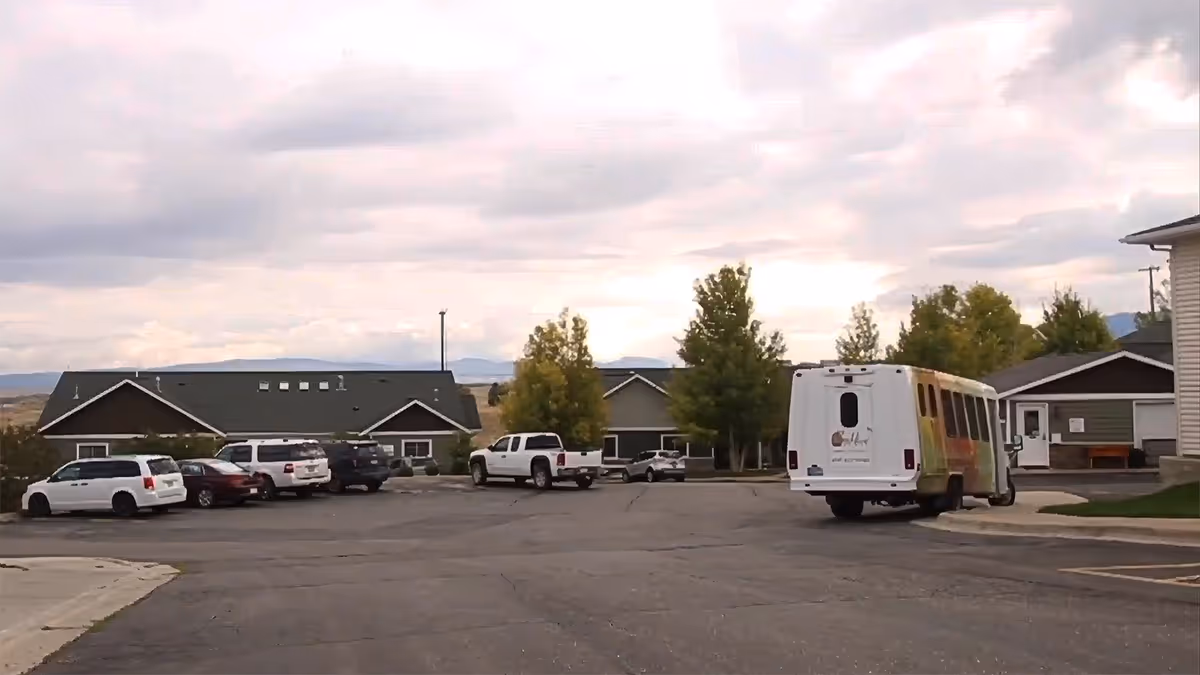 Exterior view of a senior living campus with a bus and parked cars in front.