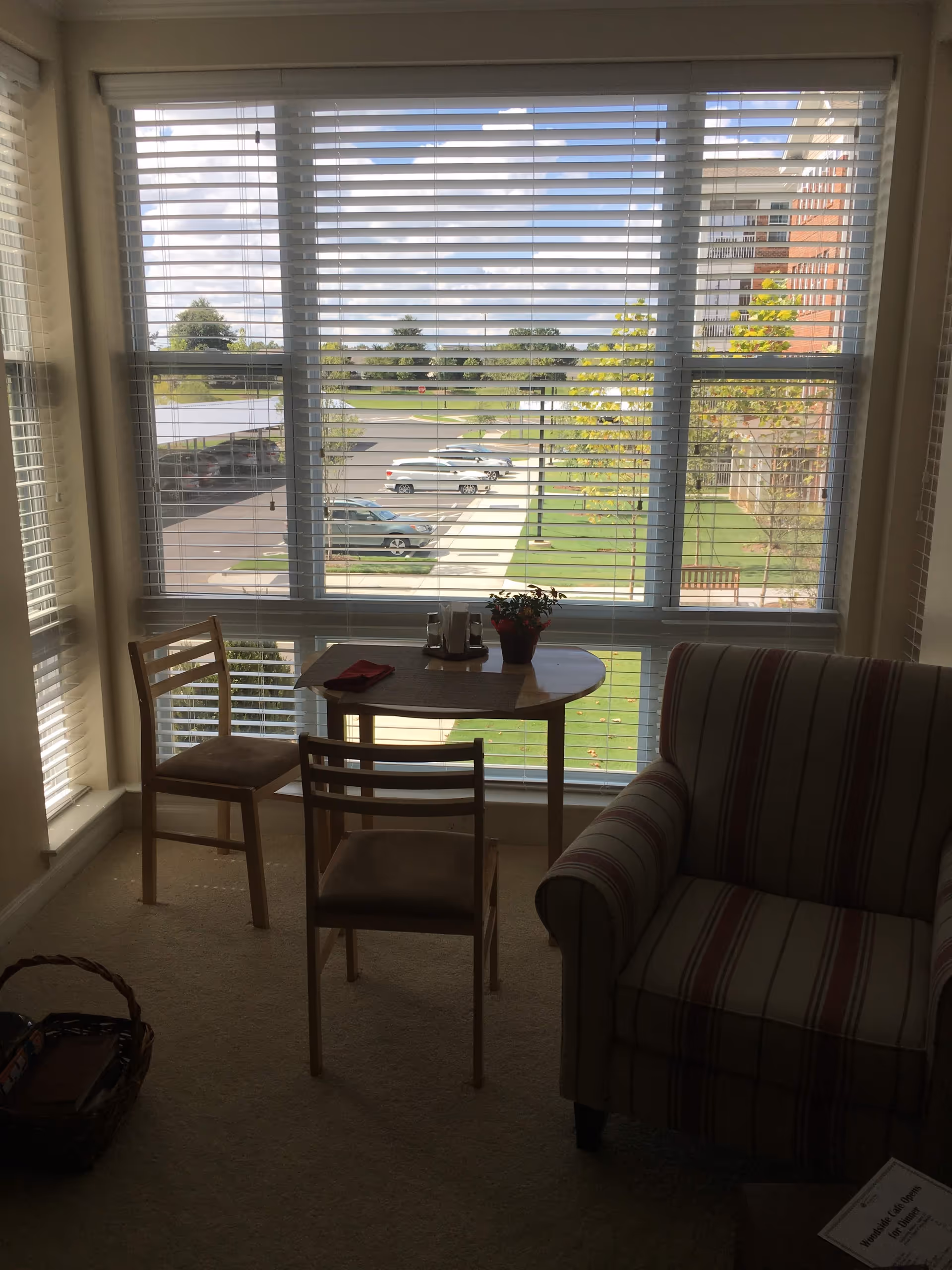 Sunlit living area with a table, two chairs, and a striped sofa near a large window.