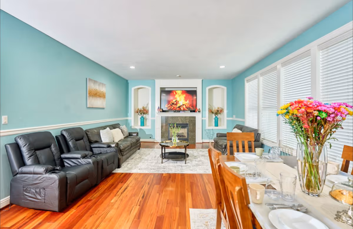 Bright teal-walled living room with leather seating, fireplace, TV, and dining area.