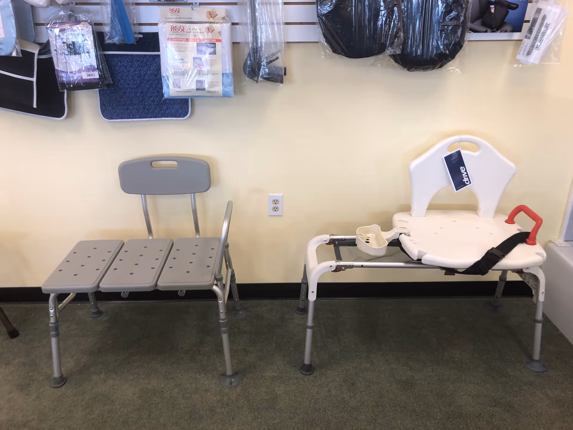 Indoor display of mobility aids: gray perforated bench and white shower chair in a showroom.
