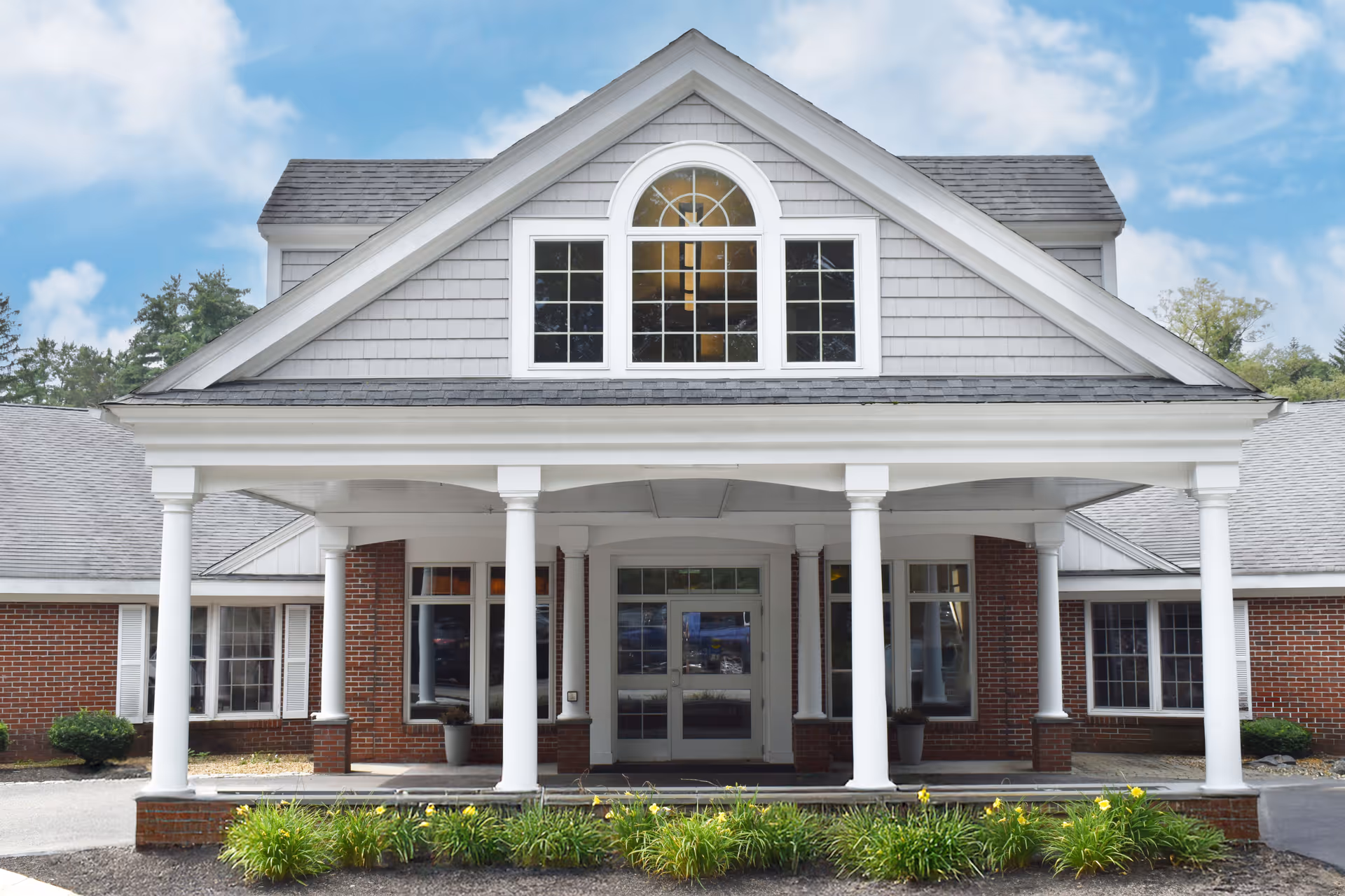 Front view of a brick senior living facility with columns and an arched window.