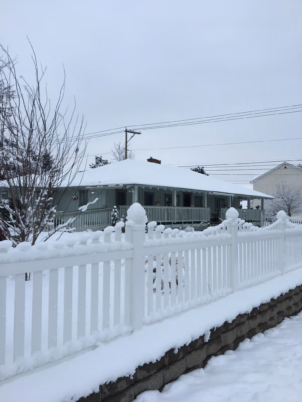 Snow-covered, single-story senior housing building with a white picket fence in front.