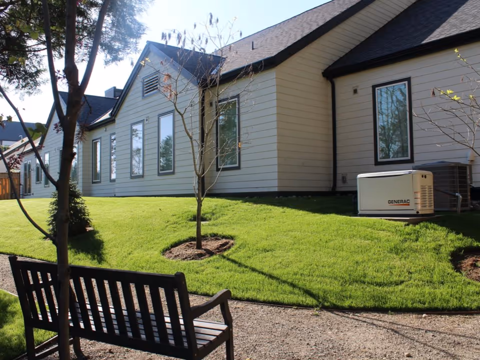 Exterior view of The Cottages of Covington with gray siding and a bench on green lawn.
