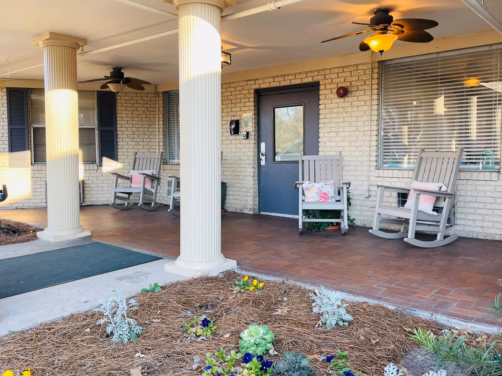 Covered brick porch at The Bluffs Rehabilitation and Healthcare Center with rocking chairs and columns.