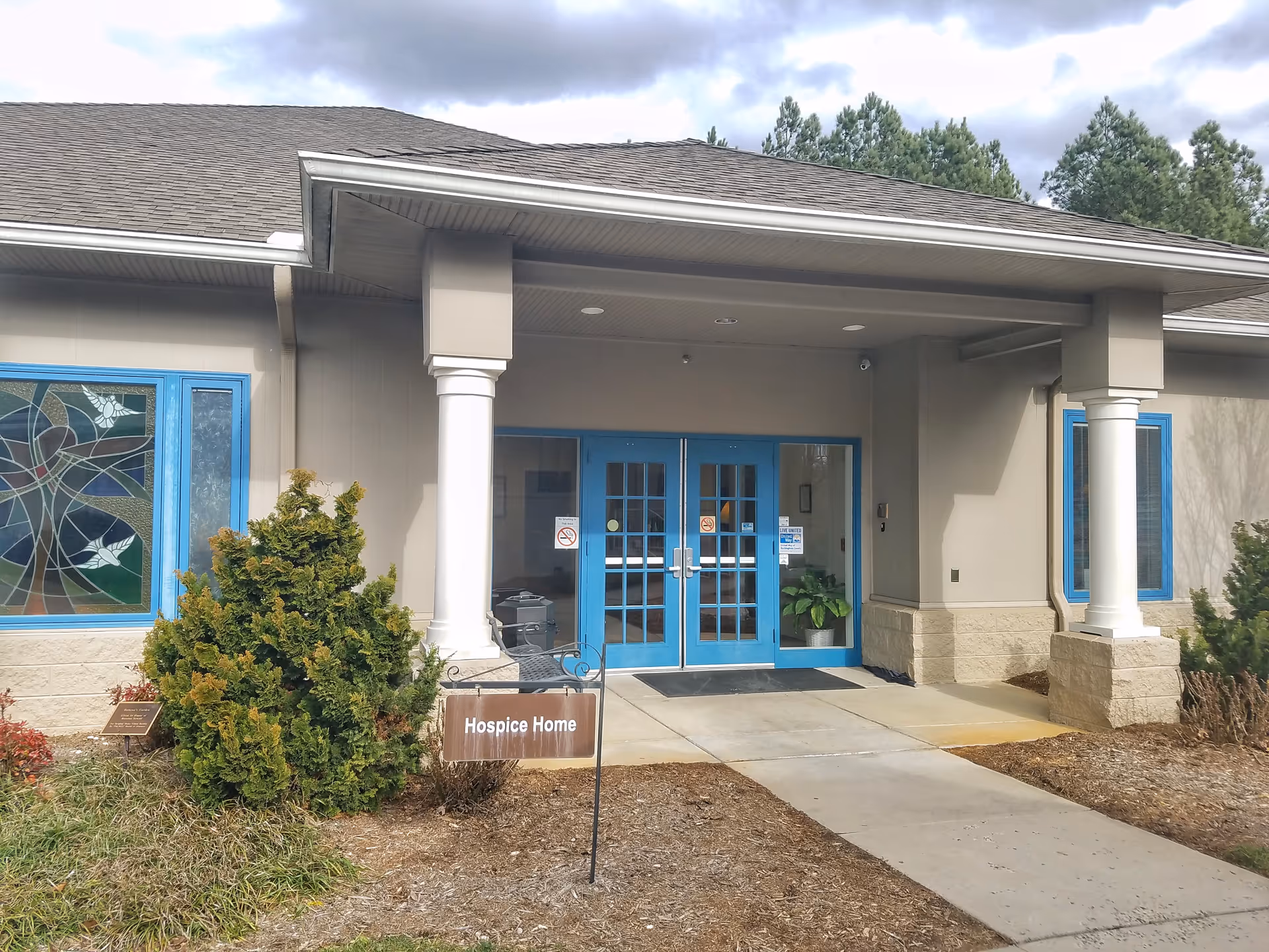 Exterior view of a building entrance with blue doors, columns, and a Hospice Home sign.