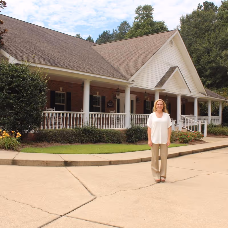 Smiling woman stands on the front walkway of Covington Ridge Retirement Home's porch.