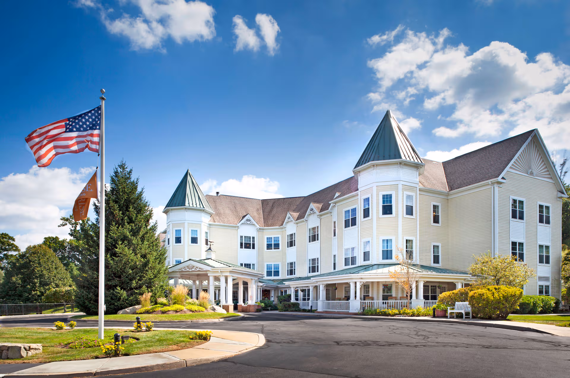 Sunrise of Cohasset exterior view of a large, light-yellow senior living building with flags.