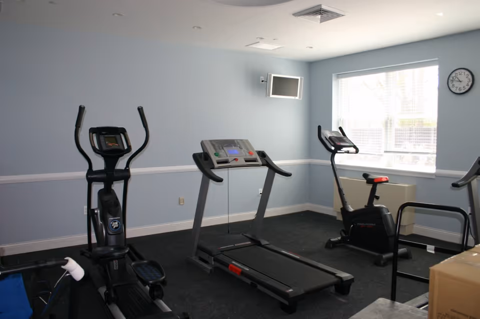Indoor fitness room with treadmills, elliptical, and stationary bike against pale blue walls.