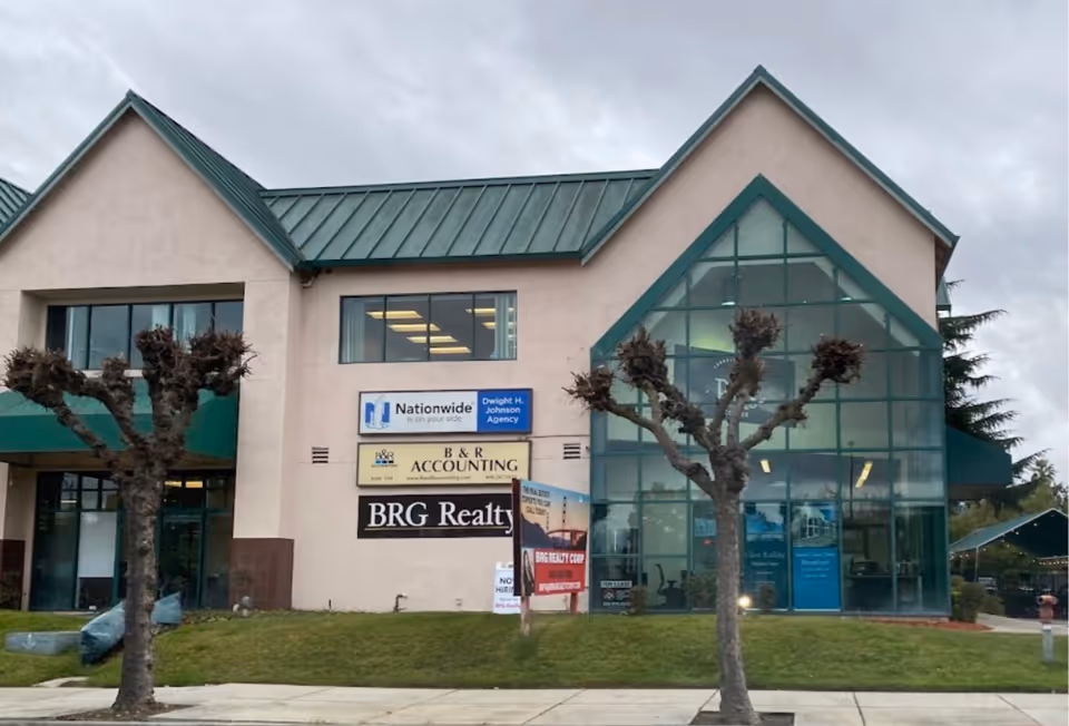 Two-story building with a glass front and multiple storefront signs outside.
