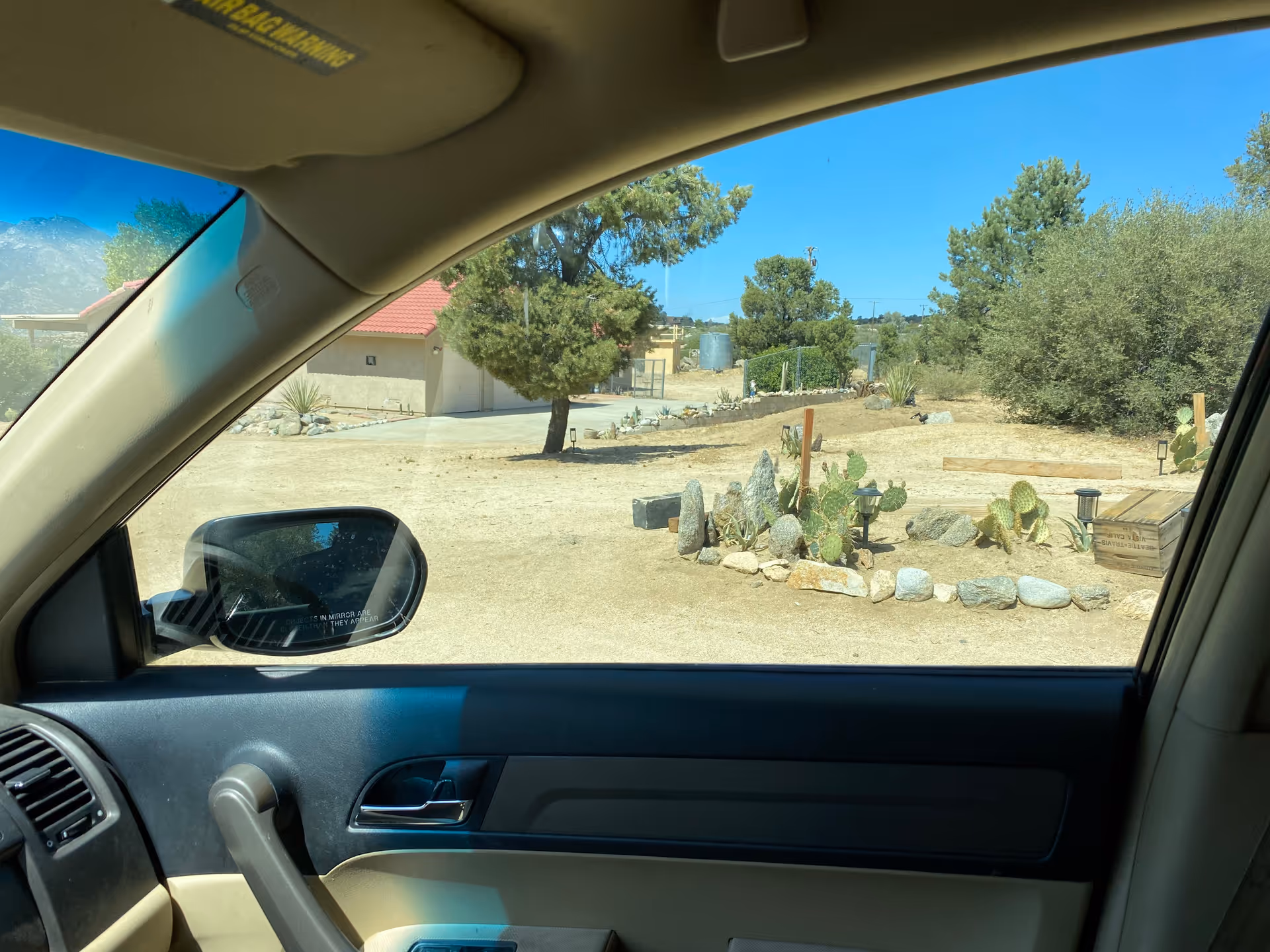 Car interior frames a desert facility yard with rocks and cacti.