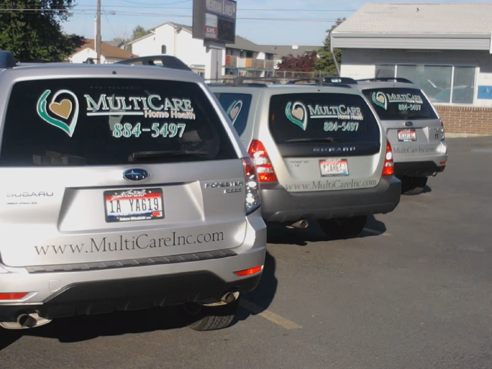 Three MultiCare branded vans parked in a lot outside a building.