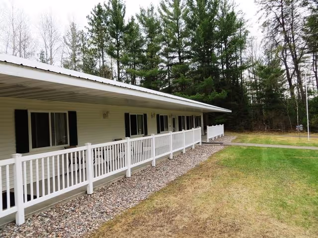 Single-story facility exterior with a long white porch, railing, and surrounding lawn.
