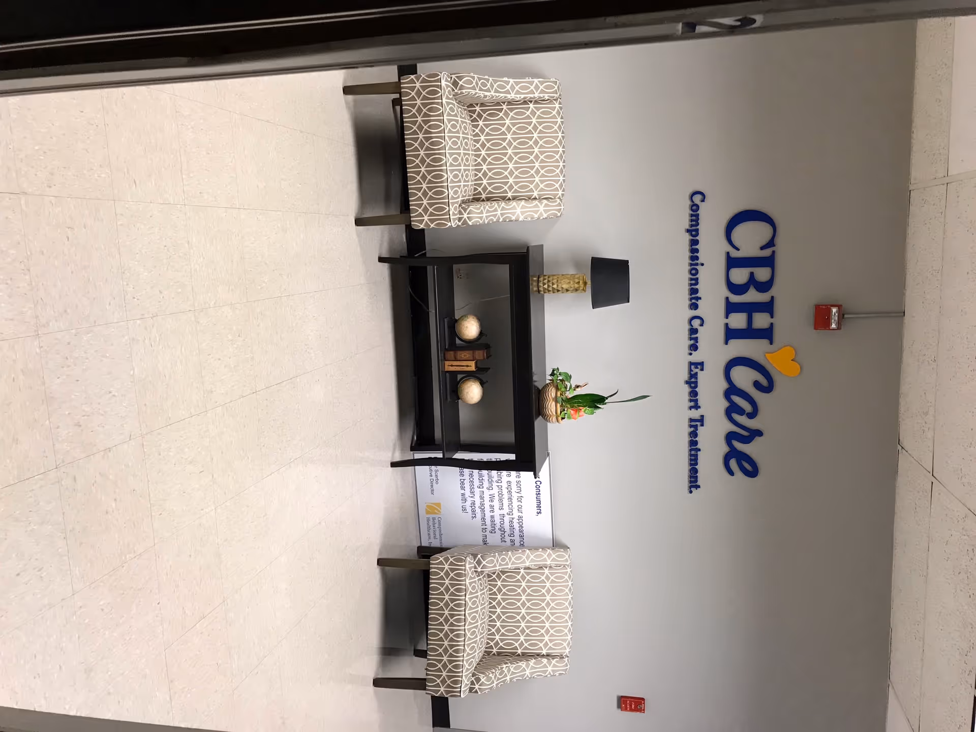 Interior waiting area with two patterned armchairs, a black coffee table, and a CBH Care sign.