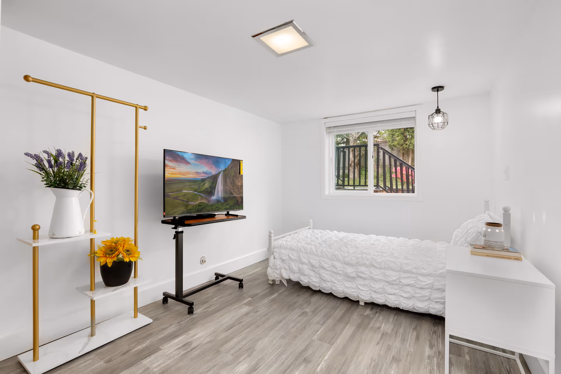 Bright, minimalist bedroom with white furniture, bed, TV, and sunny window.