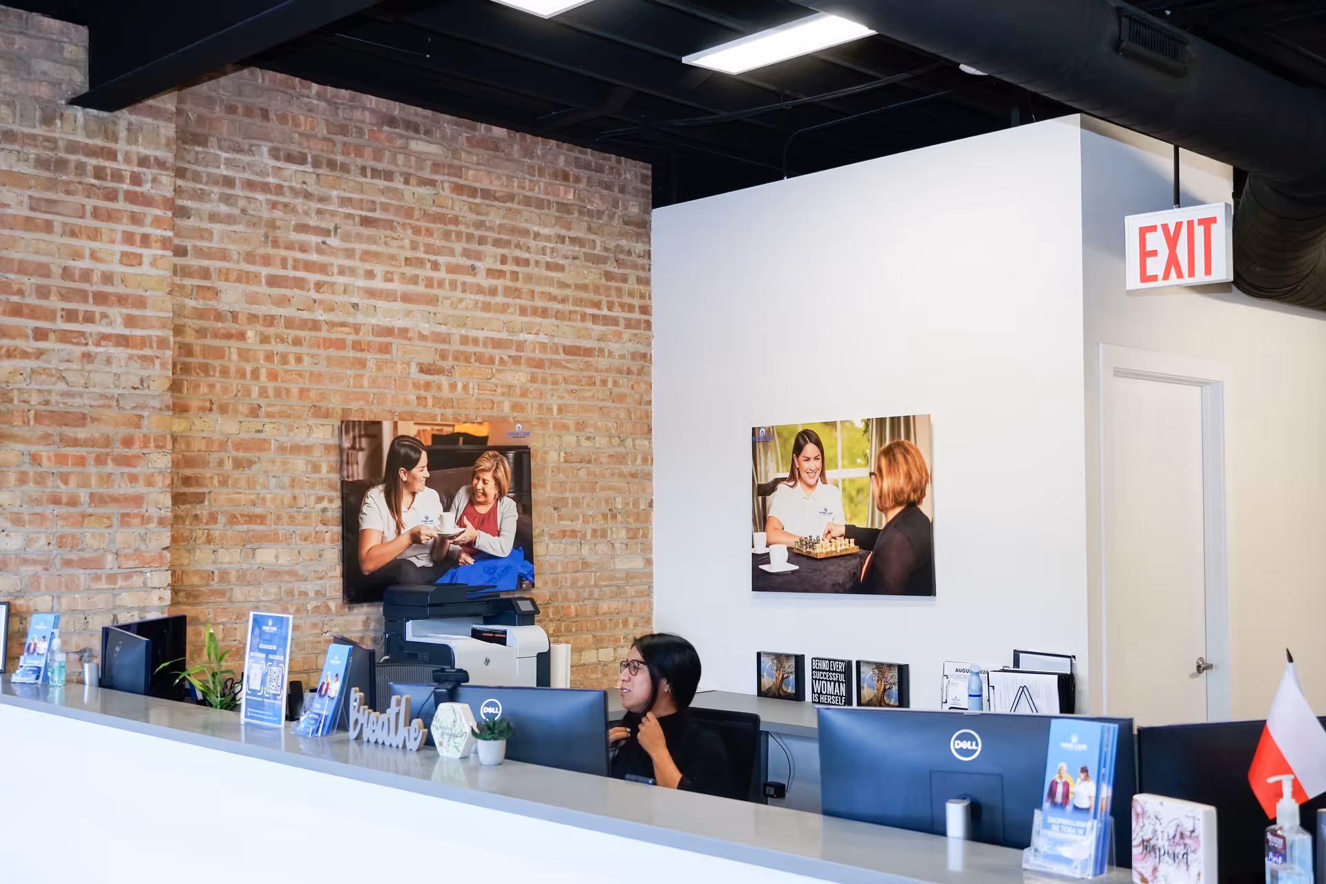 Reception desk with computer in brick-walled interior lobby; exit sign visible.