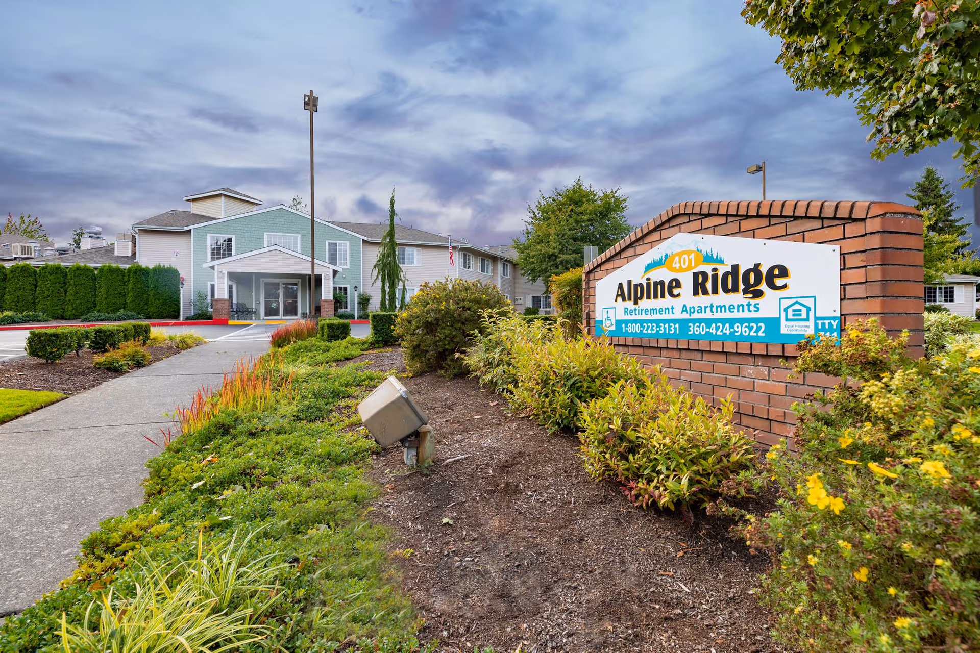 Exterior view of Alpine Ridge Retirement Apartments with sign, walkway, and manicured landscaping.
