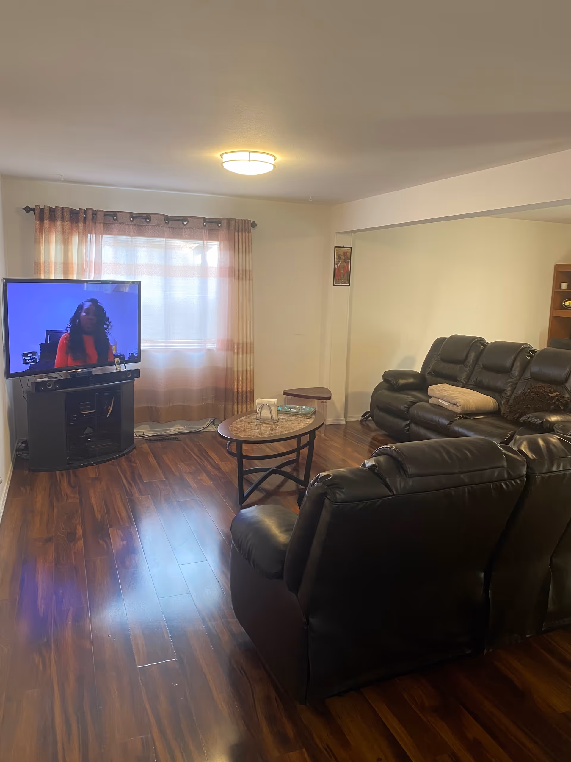 Cozy living room with leather seating, a coffee table, TV, and curtained window.