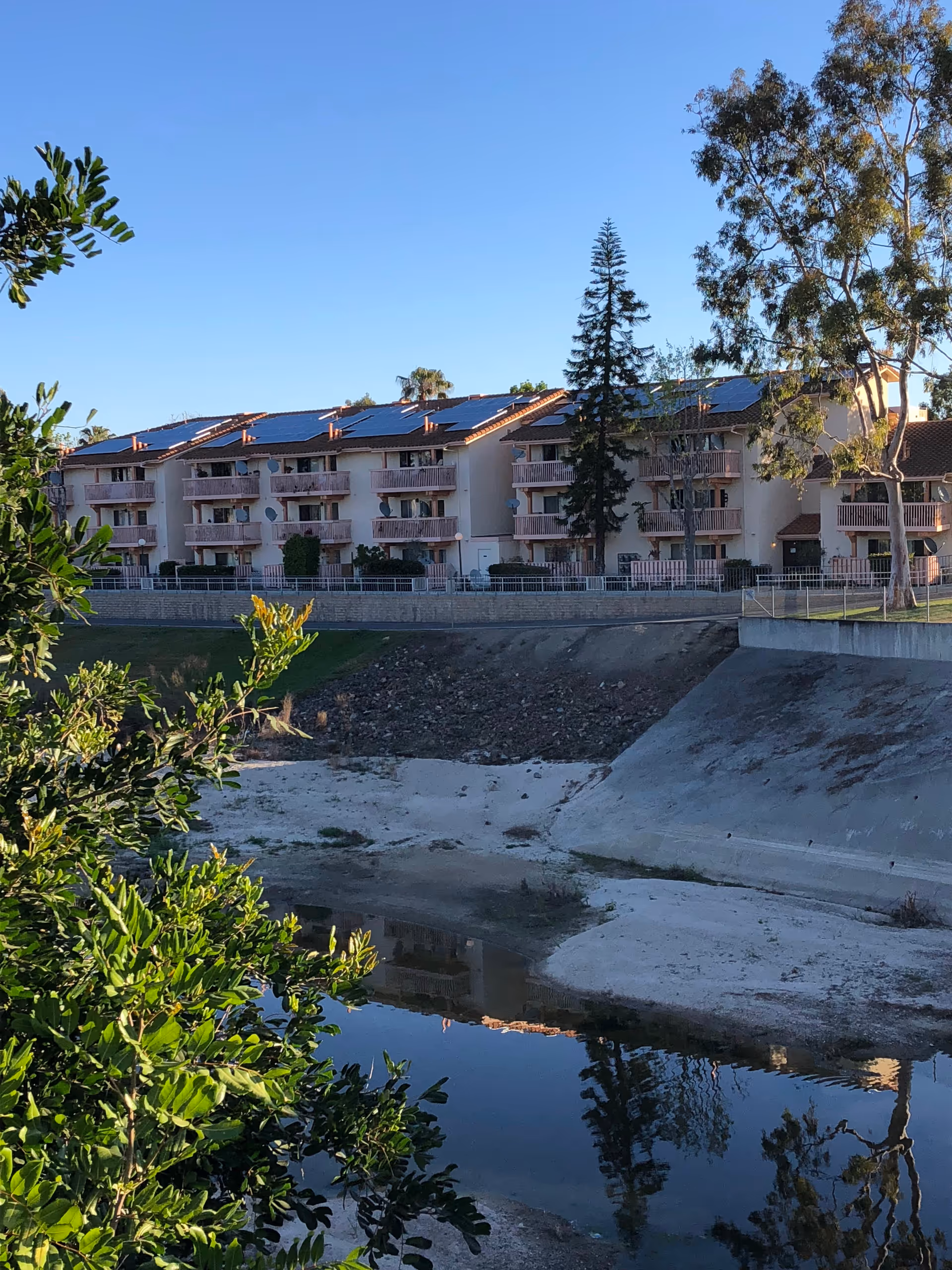 A row of beige senior-living apartments with balconies, solar panels, beside a water-filled canal.
