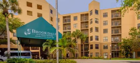 Exterior view of Brookdale Palm Beach Gardens with a green canopy entrance and palm trees