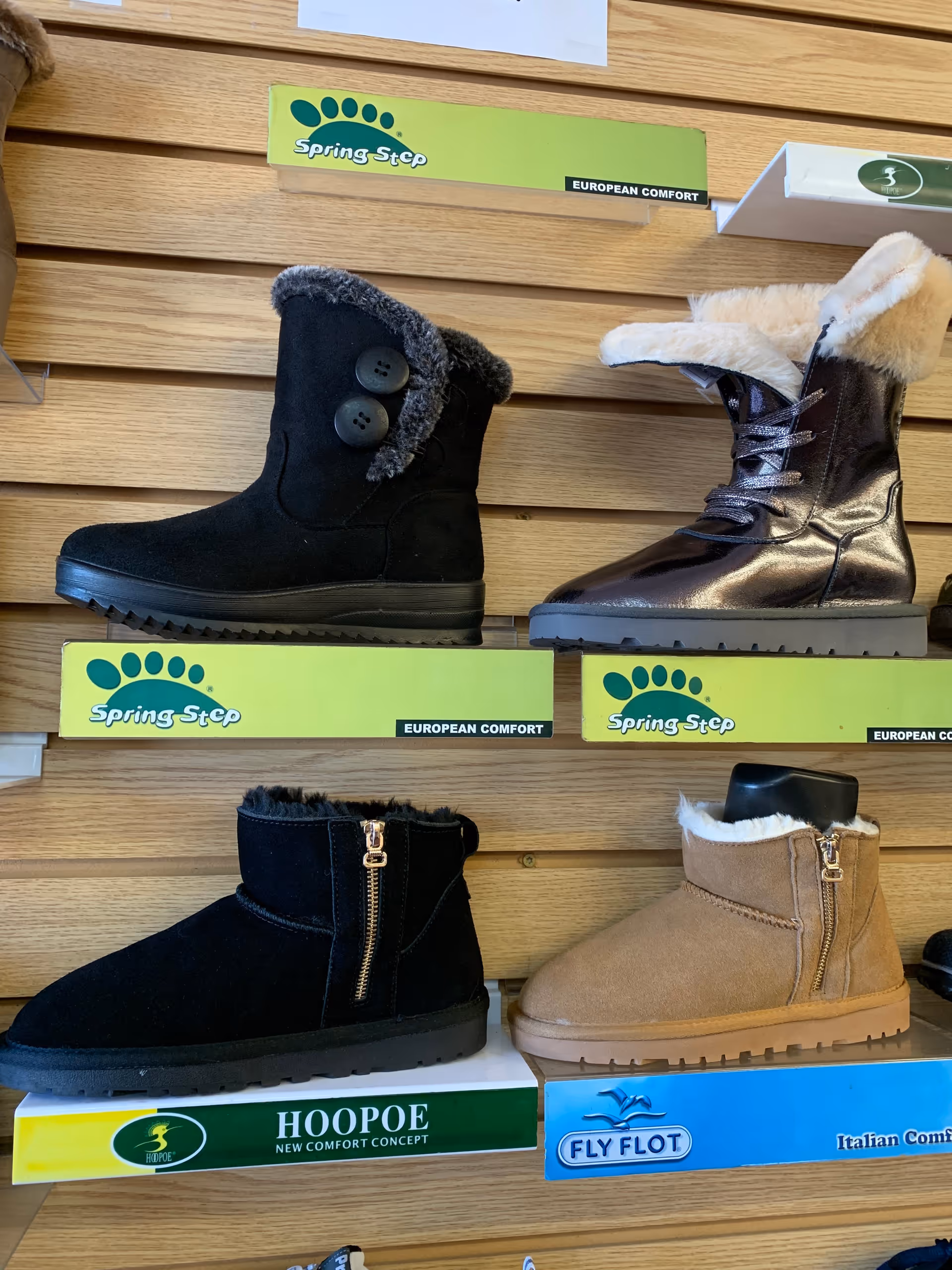 Shoe display in a store featuring winter boots on wooden shelves with brand boxes