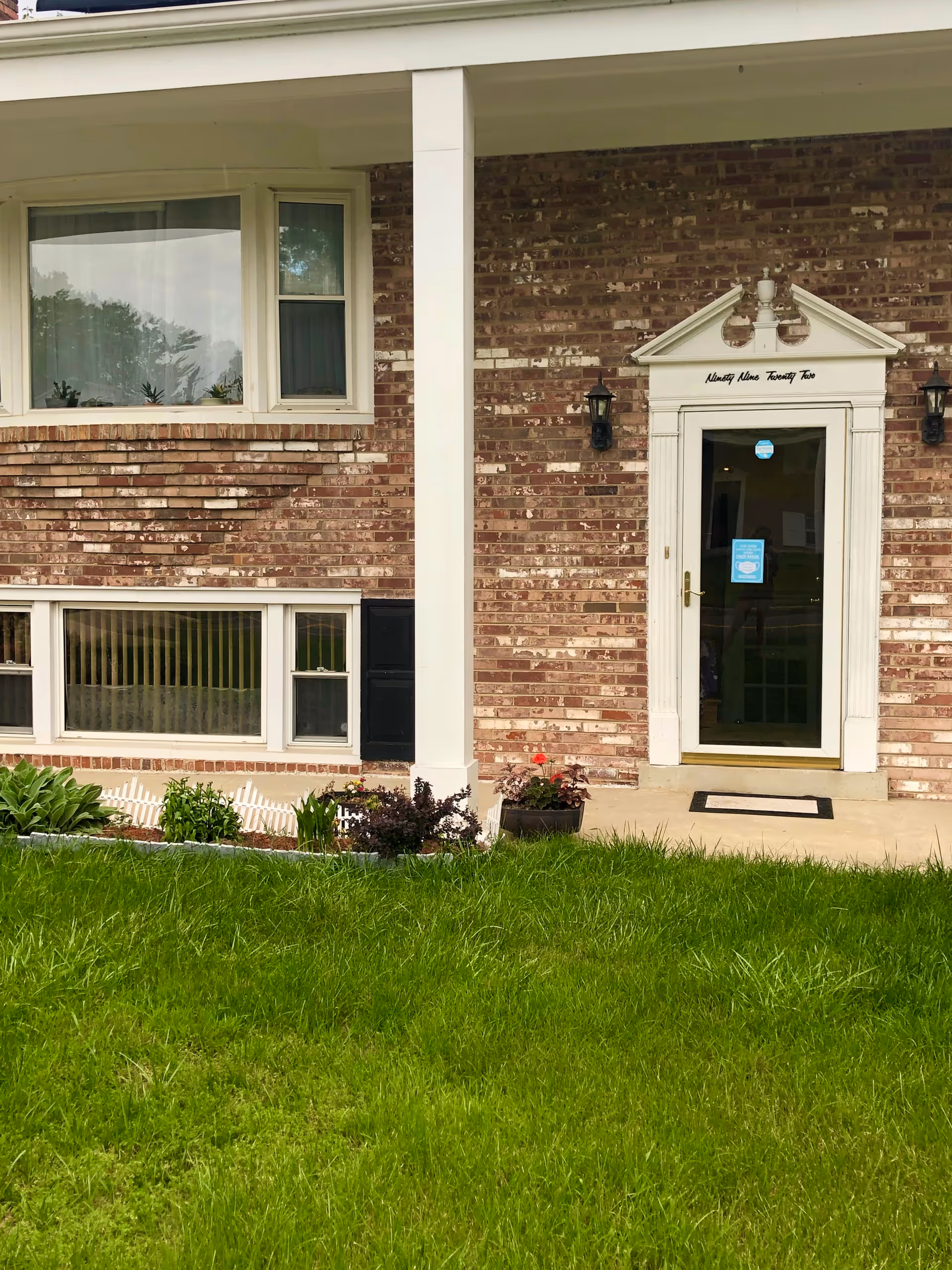 Front entrance of a brick assisted living building with a white column, windows, and lawn.