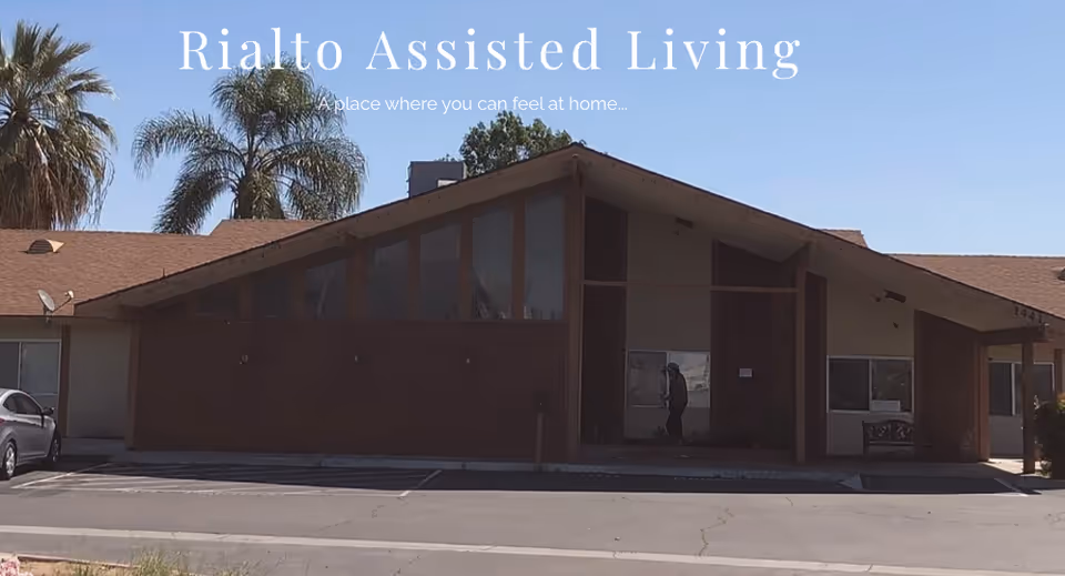 Front exterior of Rialto Assisted Living facility with large windows and a person near entrance.