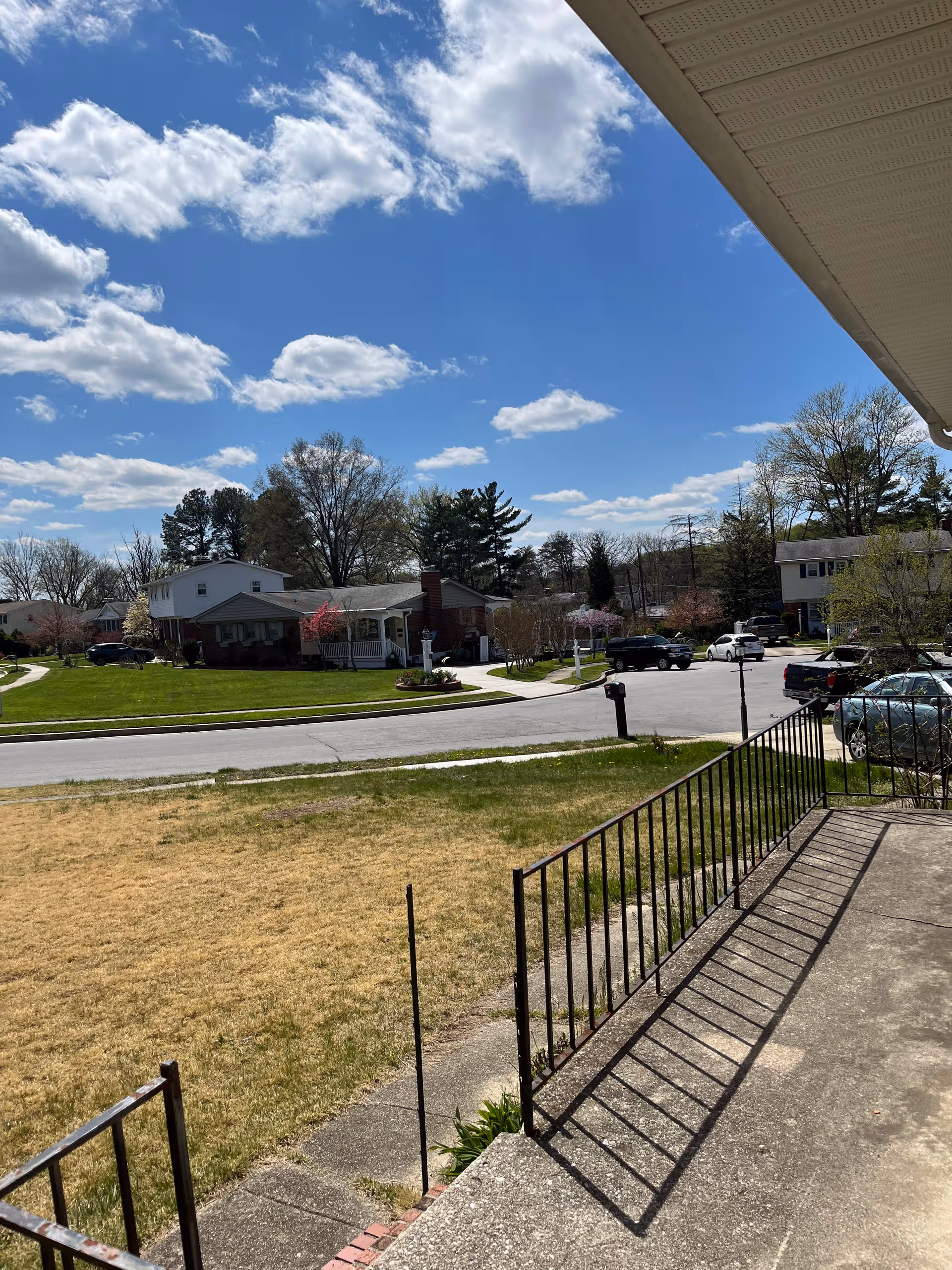 Exterior view from a porch shows a street with houses, trees, and parked cars.