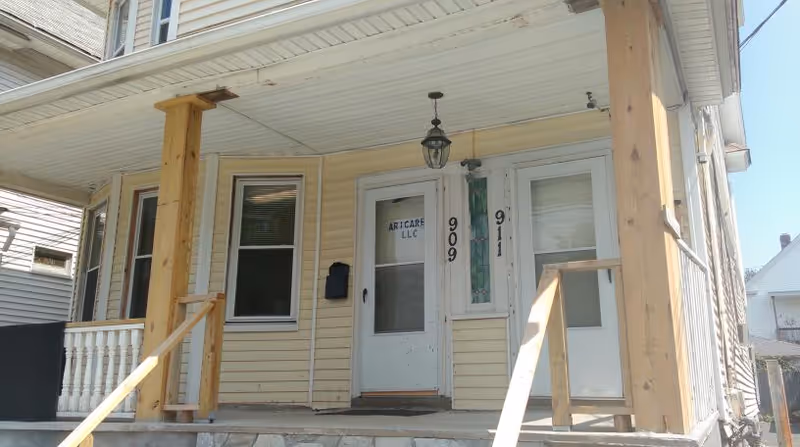 Beige house-style building with a porch, wooden posts, and a front door labeled Aricare LLC