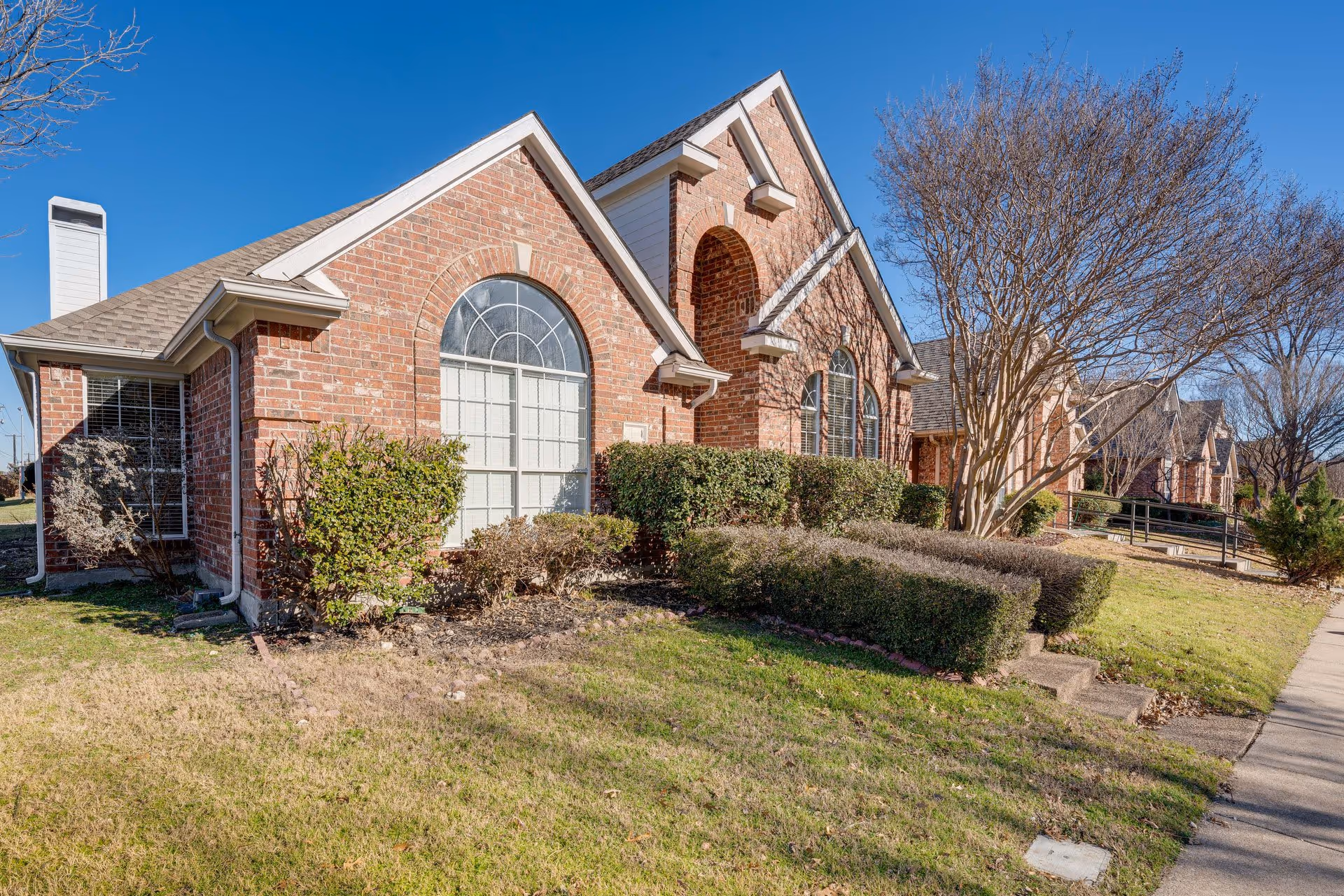 Brick-fronted assisted living facility with arched windows, shrubs, and a sidewalk.