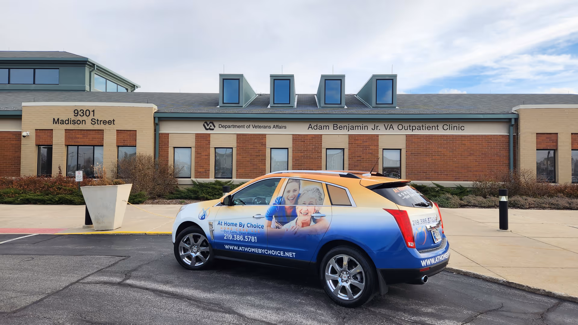 Exterior view of brick clinic building with a VA Outpatient Clinic sign and a promotional car.