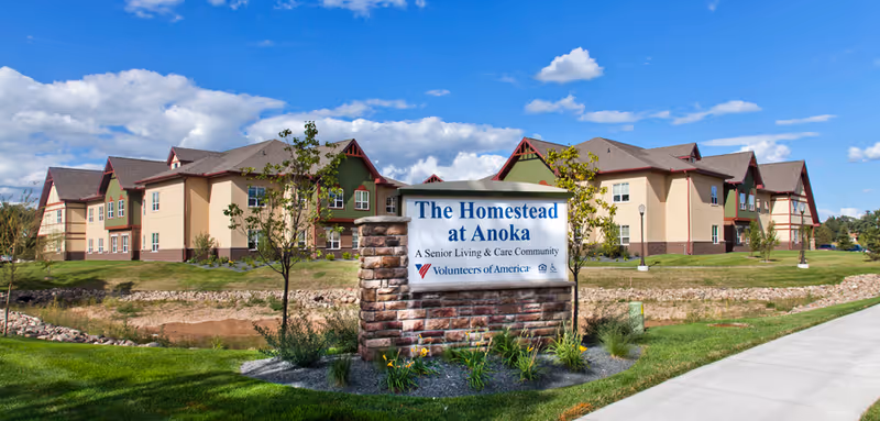 Exterior view of The Homestead at Anoka senior living facility with a stone sign.
