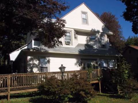 White two-story house with a wooden deck and lamp on a sunny front yard