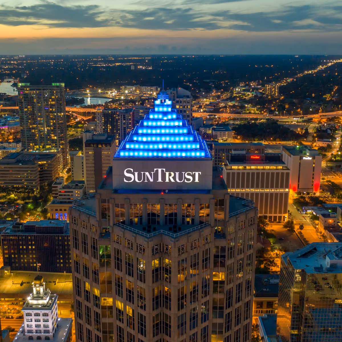 Aerial cityscape at dusk featuring a tall building with a blue-lit pyramid top SunTrust sign.