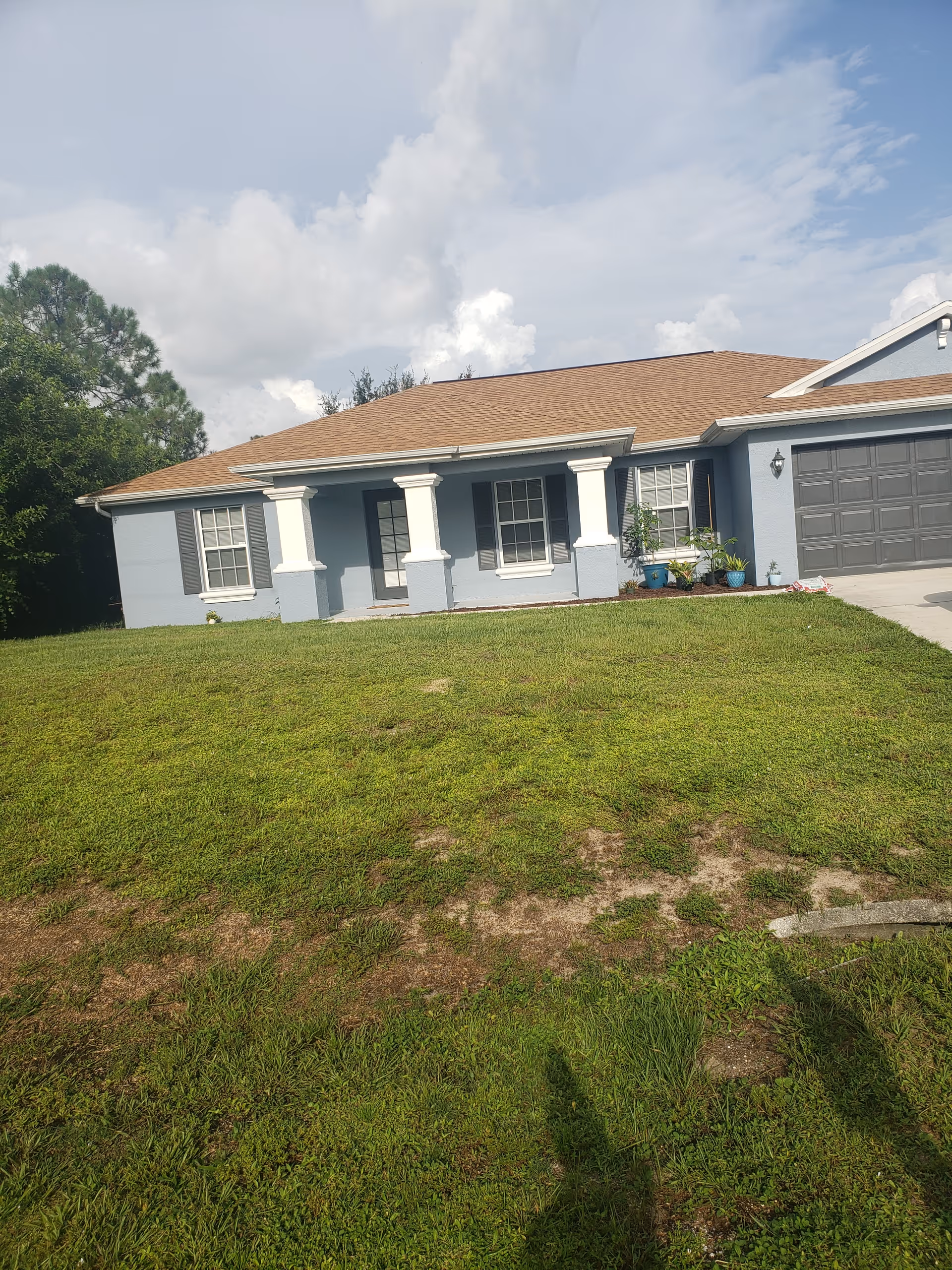 Blue single-story house with brown roof, front lawn, and two-car garage.