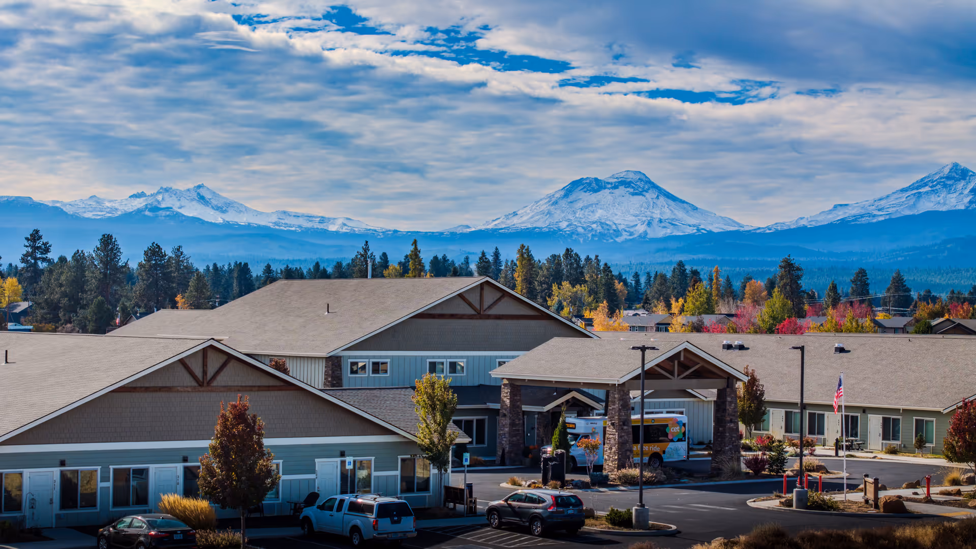 Exterior view of The Lodge Retirement Community with a covered entrance, parking, and distant mountains.