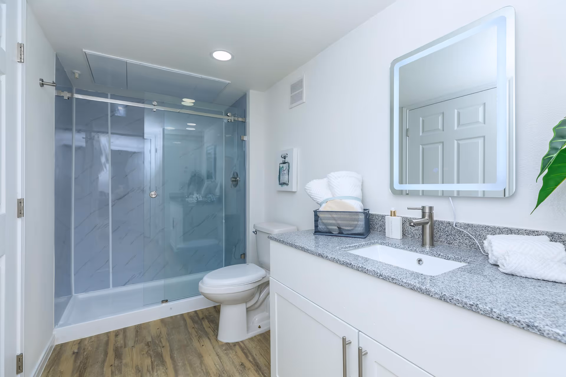 Modern bathroom with glass shower enclosure, granite counter, sink, mirror, and toilet.