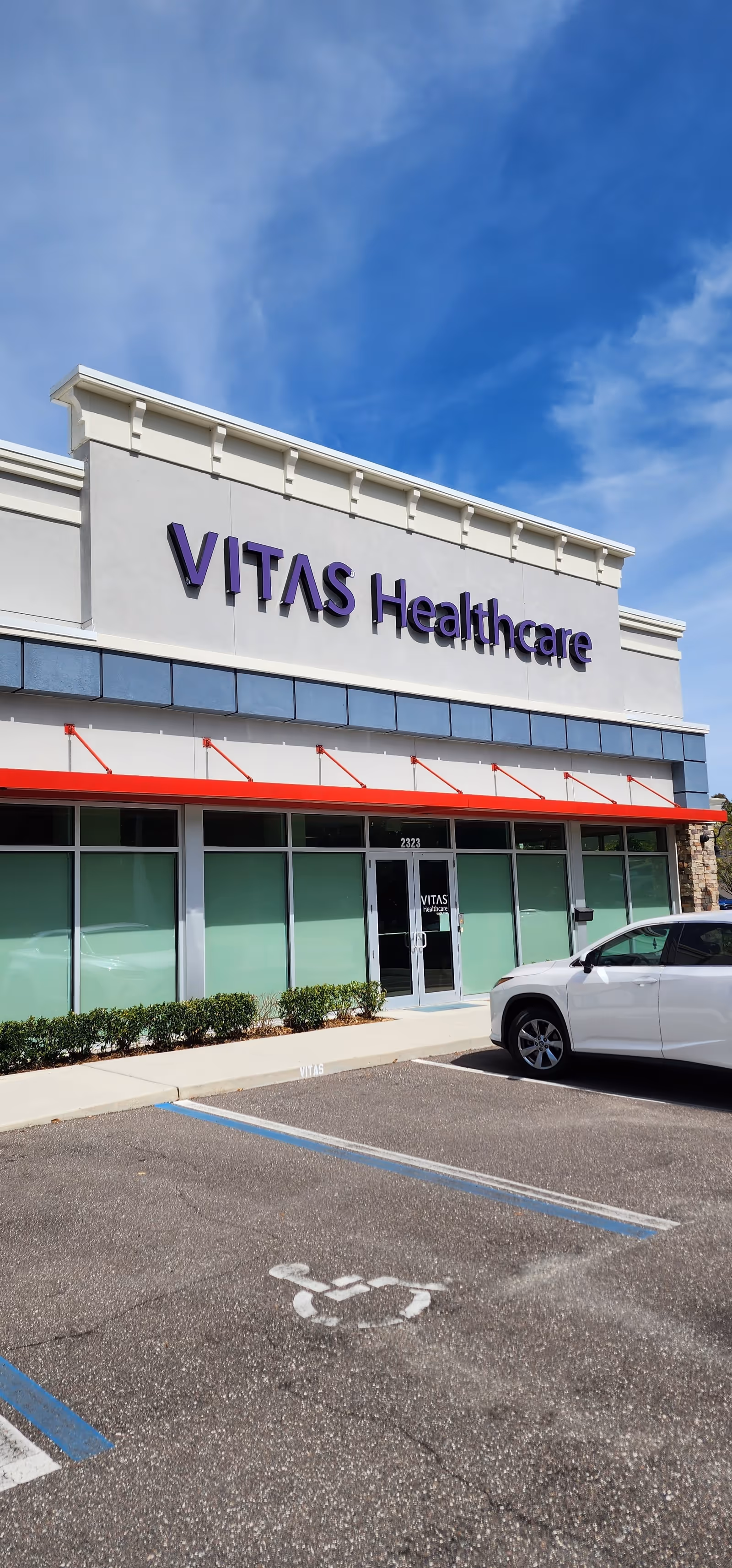 Exterior view of VITAS Healthcare building with glass doors and a parking lot.