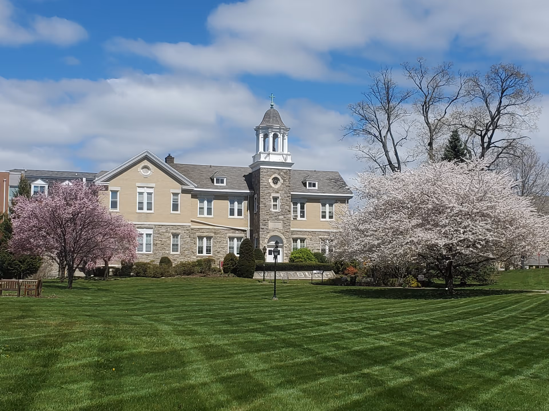 Large two-story building with a central cupola, manicured lawn, and blooming trees.